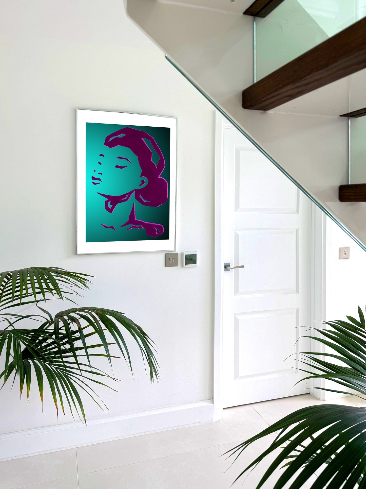 Modern interior with a framed artwork of a woman's face on a white wall, surrounded by plants.