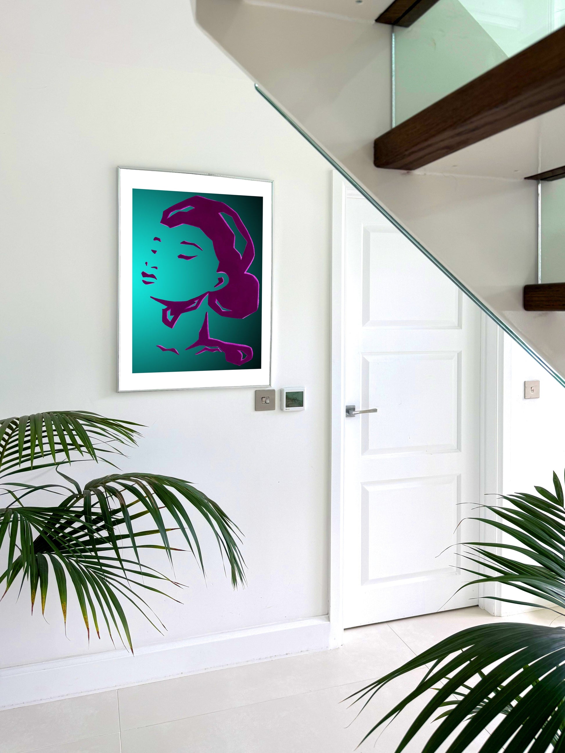Modern interior with a framed artwork of a woman's face on a white wall, surrounded by plants.