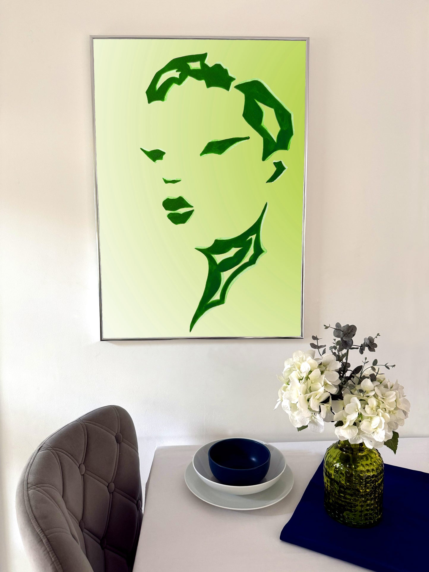 Framed green silhouette art on a wall above a table with decorative items.