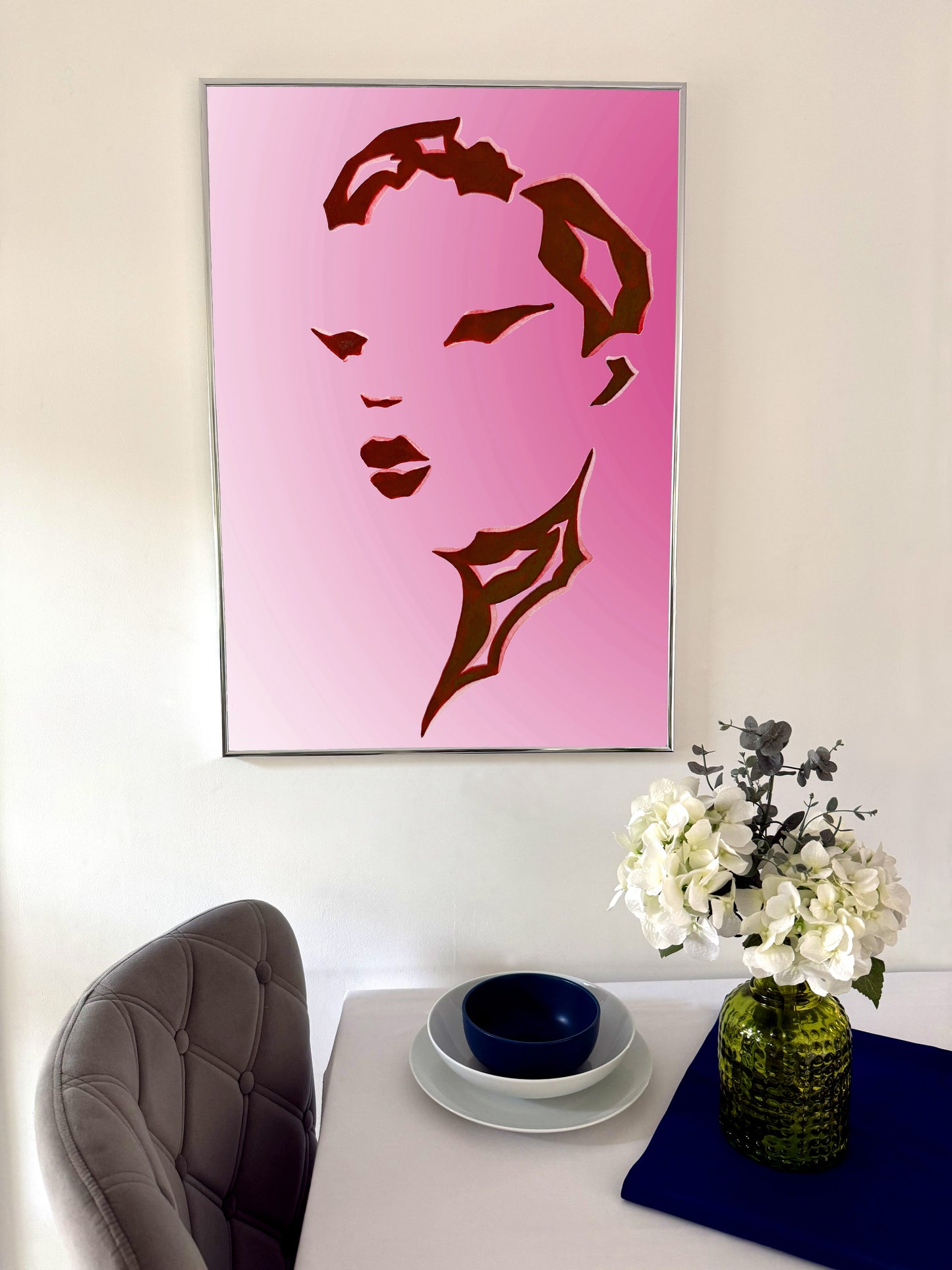 Pink artwork of a stylized face on a wall above a dining table with a vase and flowers.