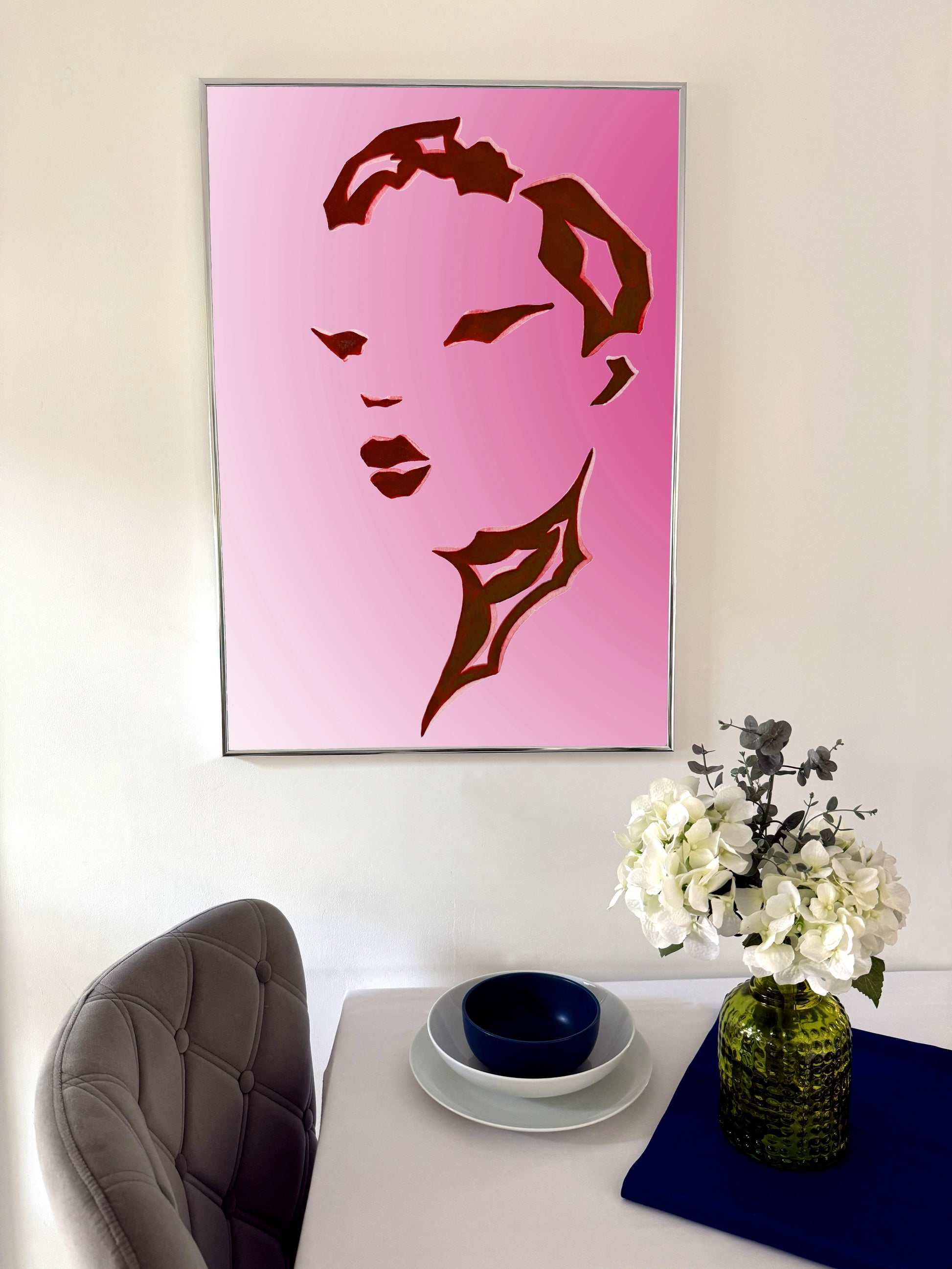Pink artwork of a stylized face on a wall above a dining table with a vase and flowers.