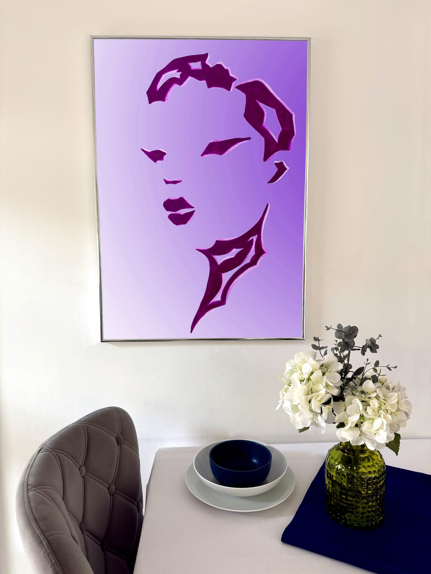 Framed purple portrait on a wall above a table with decorative items.